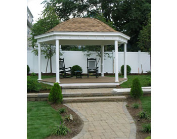 12 x 16 Vinyl Elongated Hexagon Belle Gazebo shown with Saddle Color Trex Decking, 6" Vinyl Smooth Columns with Square Trim, and Rustic Cedar Asphalt Shingles.