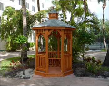 6 Treated Pine Octagon Gazebo shown with 2x2 Decorative Railings, Old English Asphalt Shingles, 2 Coats of Cedar Stain/Sealer, Hurricane Package, and 2 Bench Sections.