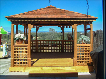 12x12 Treated Pine Gazebo shown with Custom Cupola, Custom Lattice Half-wall, Custom Lattice Corners, Cedar Stain, Wavy Fascia, Treated Pine Deck, Cedar Shake Shingles, and Two Extra Entrance Openings.